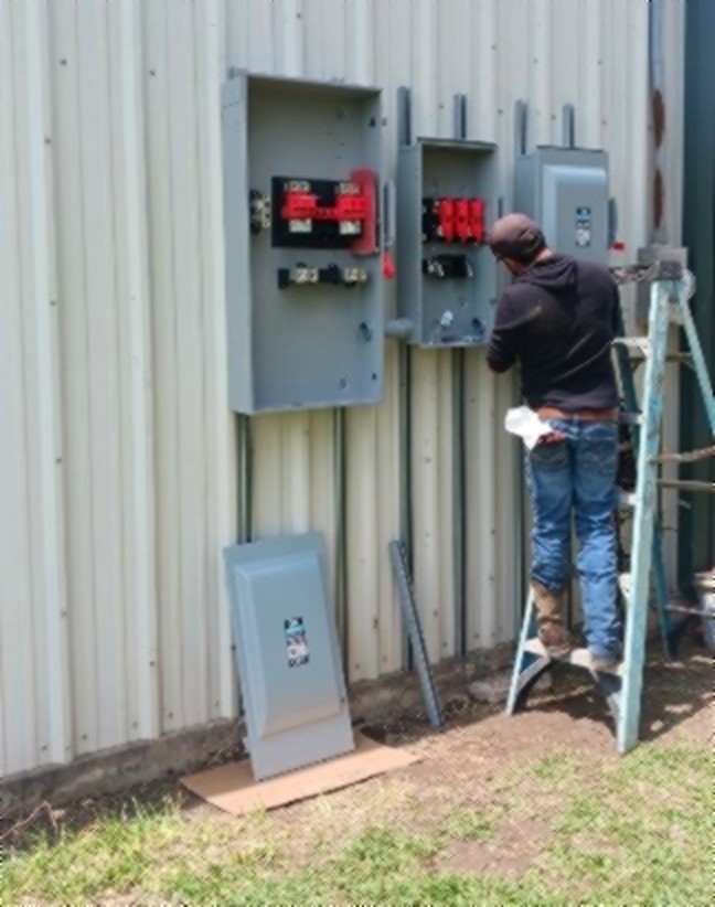 SCI Electrical electrician on a ladder wiring fused disconnects on a metal building in South Texas